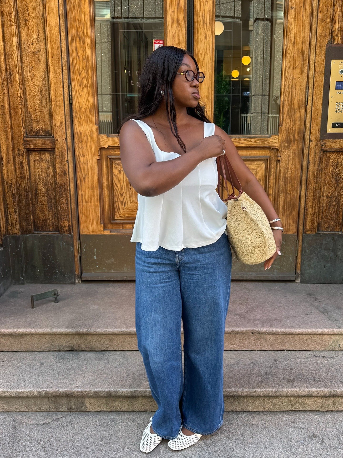Mulher posa com jeans azul de modelagem reta, blusa branca fluida e sapatilha branca de textura vazada, em clima casual
