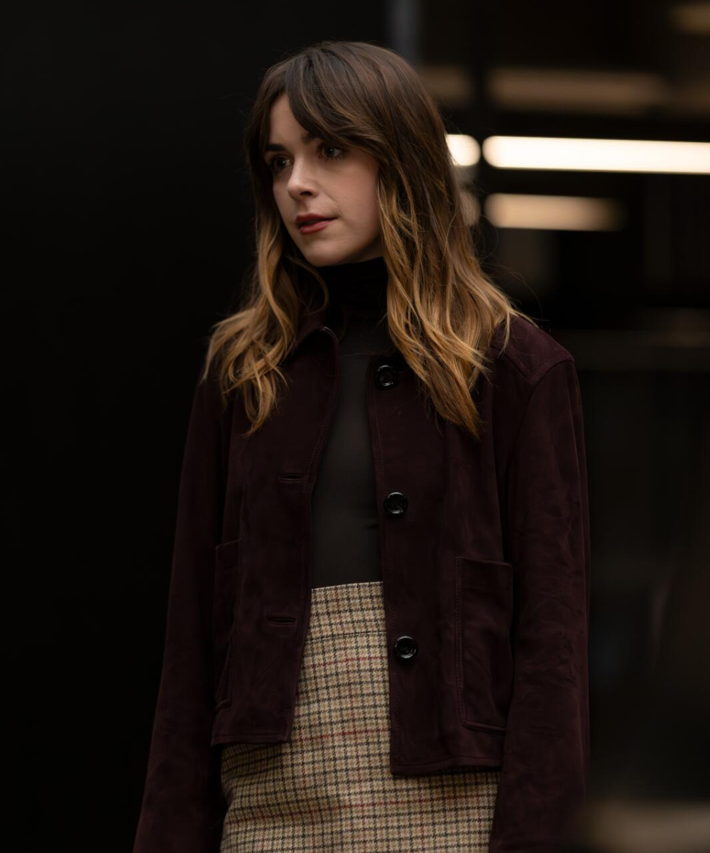 Modelo posa com jaqueta vinho de botões grandes, blusa preta justa e saia xadrez bege, expressando introspecção na quarta