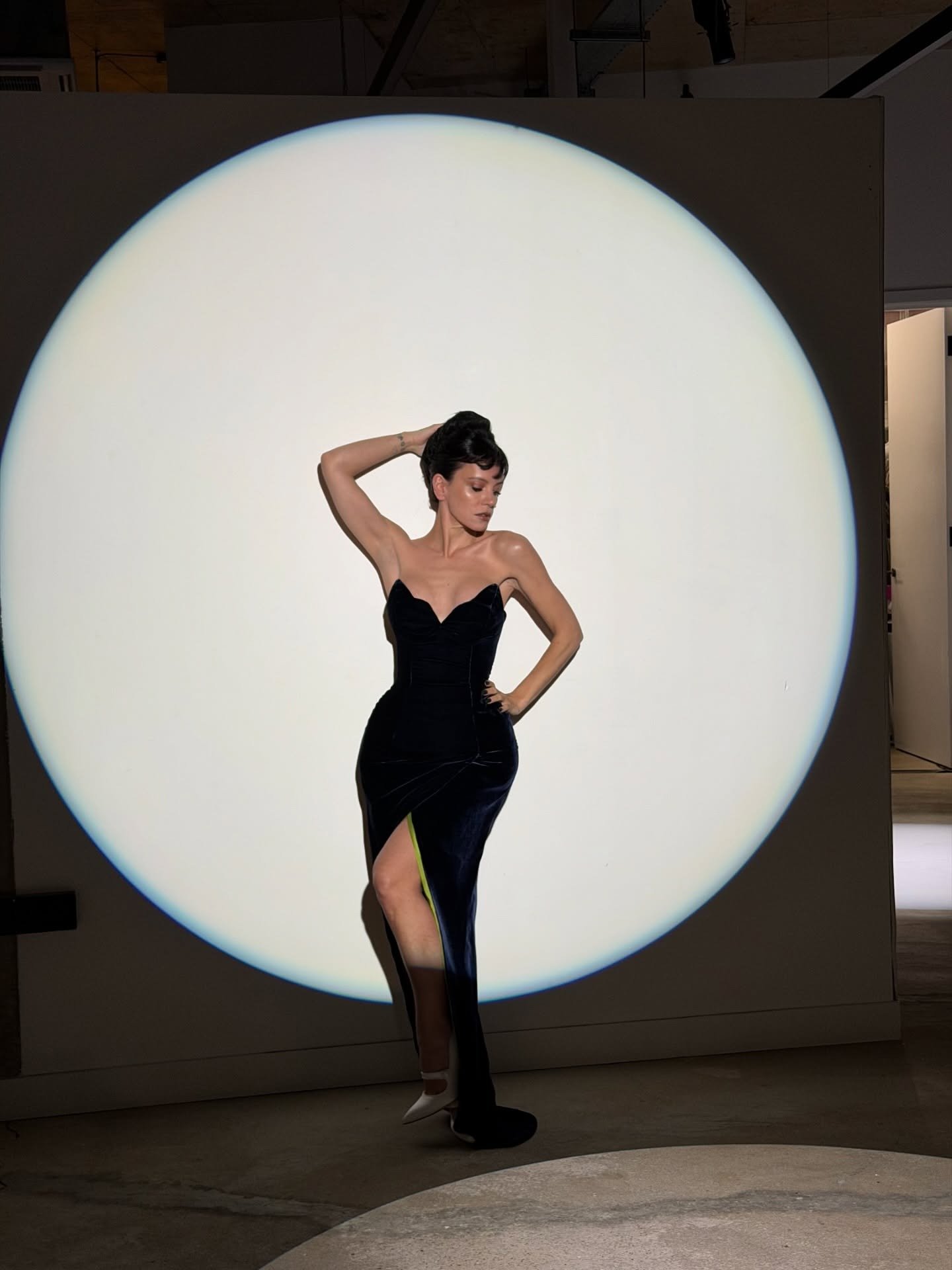 Lily Allen posa com vestido longo justo de veludo preto, decote coração e fenda lateral, em clima sofisticado e elegante.