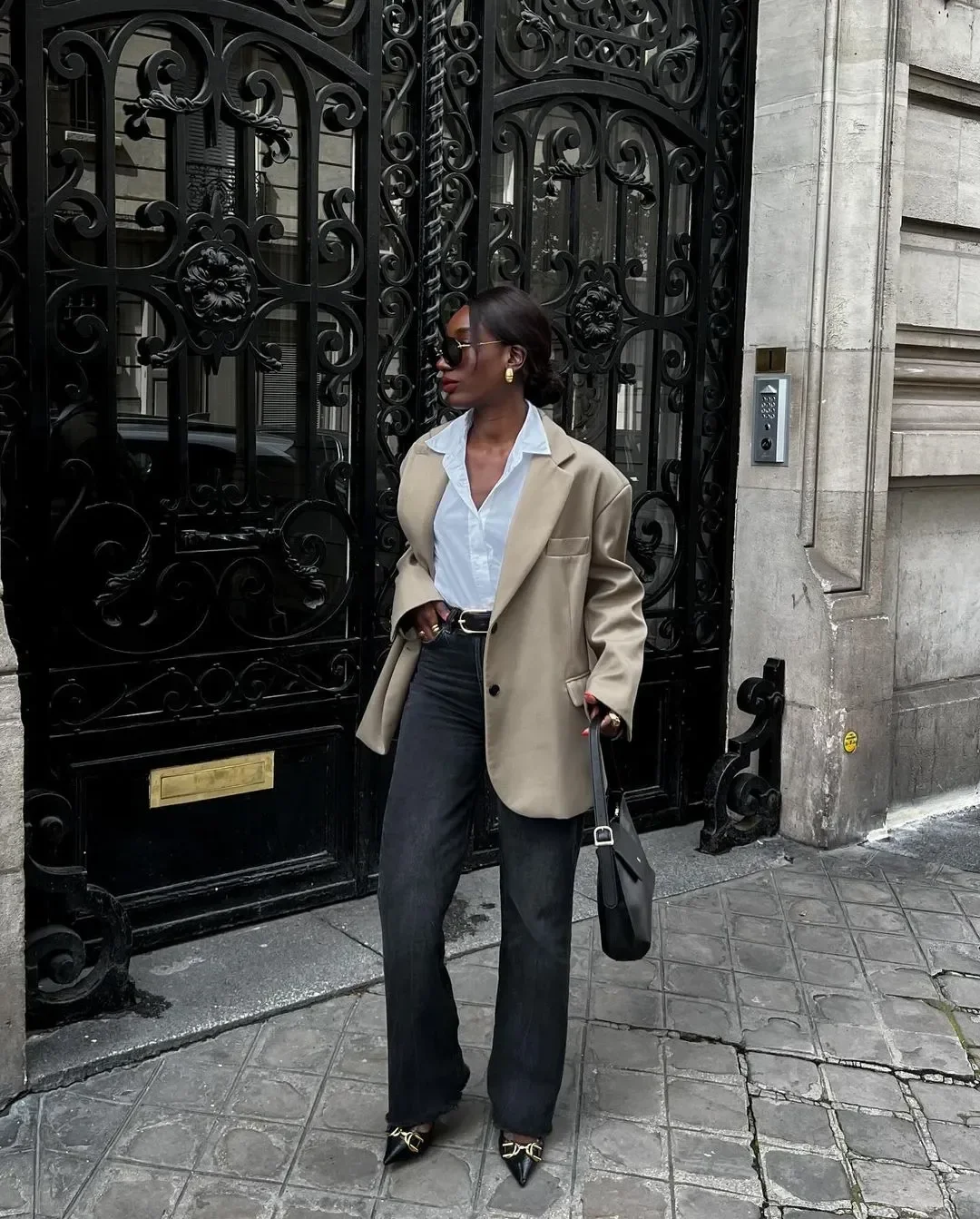 Look esporte fino feminino com calça jeans preta reta, camisa branca, blazer bege oversized, acessórios dourados e bolsa
