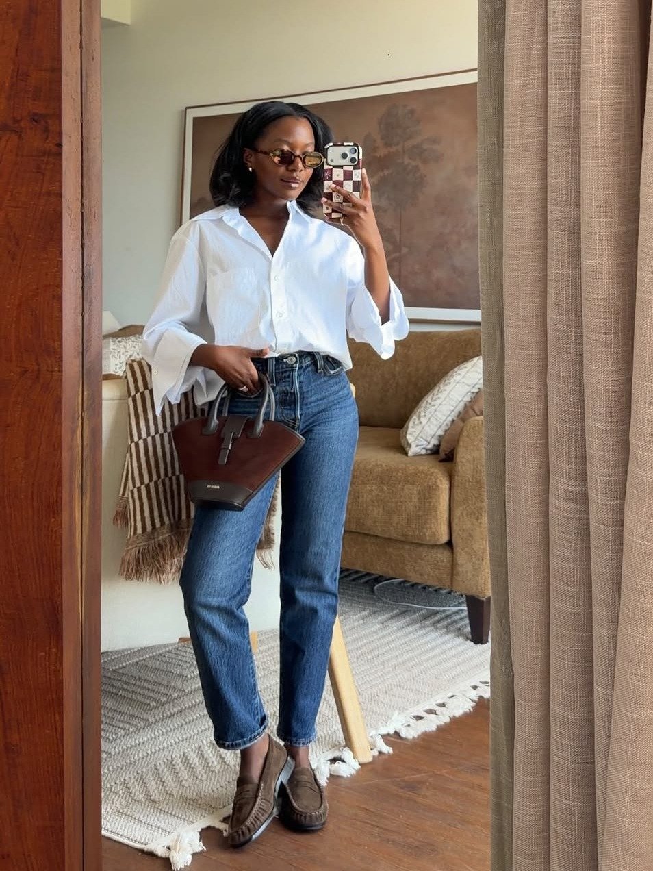 Mulher posa com look esporte fino feminino com calça jeans reta azul, camisa branca de algodão, mocassim marrom e bolsa