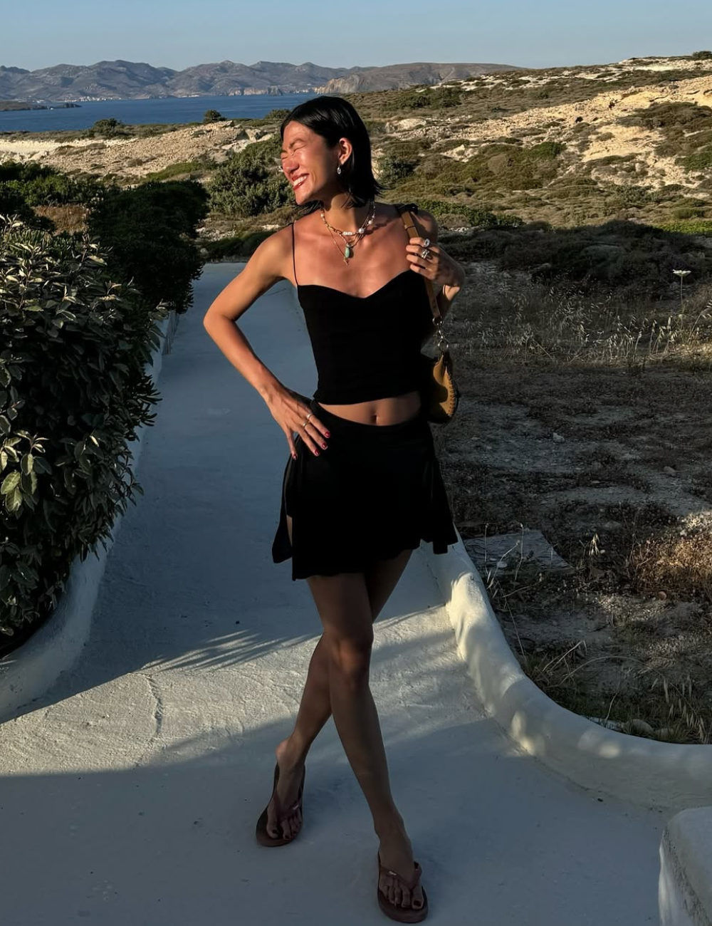 Look com minissaia preta fluida e top cropped de alças finas, combinando acessórios delicados e postura confiante.