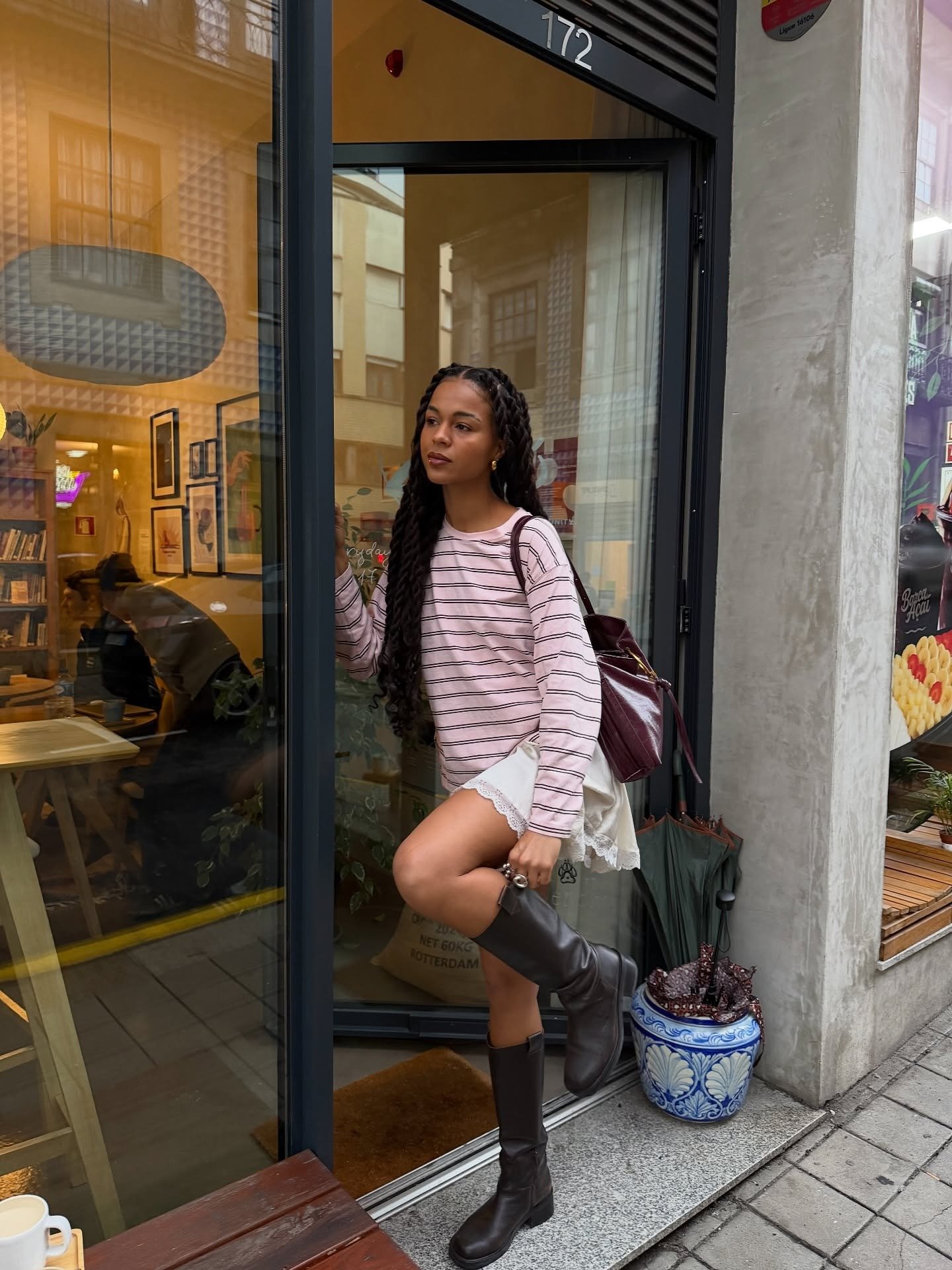 Modelo posa com looks lindos que combinam blusa rosa listrada, saia branca com renda e botas marrons de couro