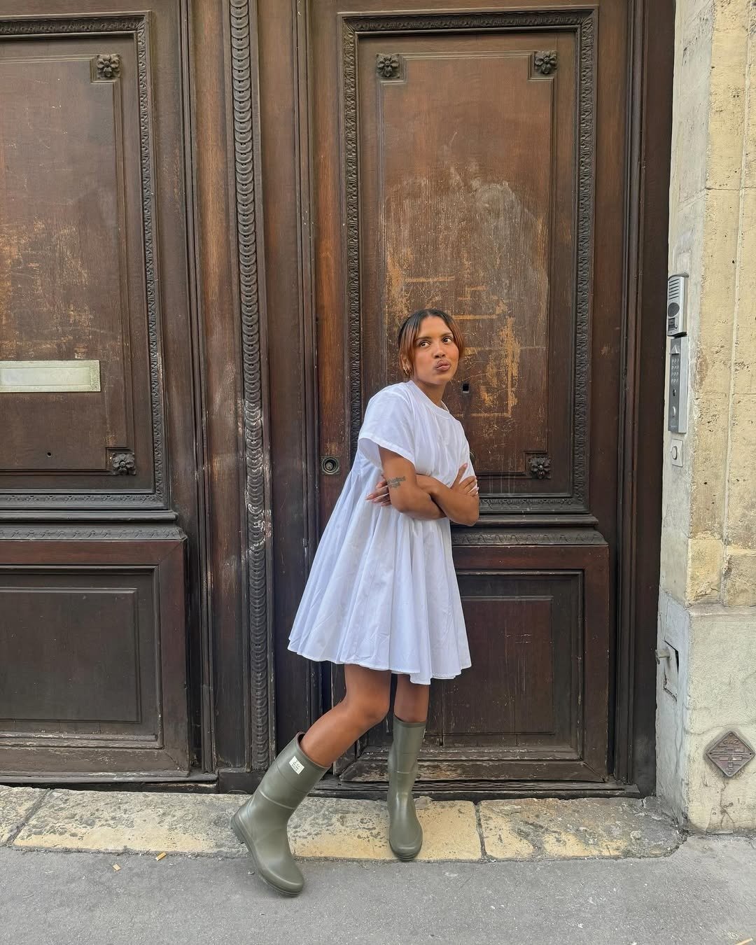 Modelo posa com vestido branco solto de algodão e botas verdes de borracha, criando looks lindos com estilo casual e urbano.