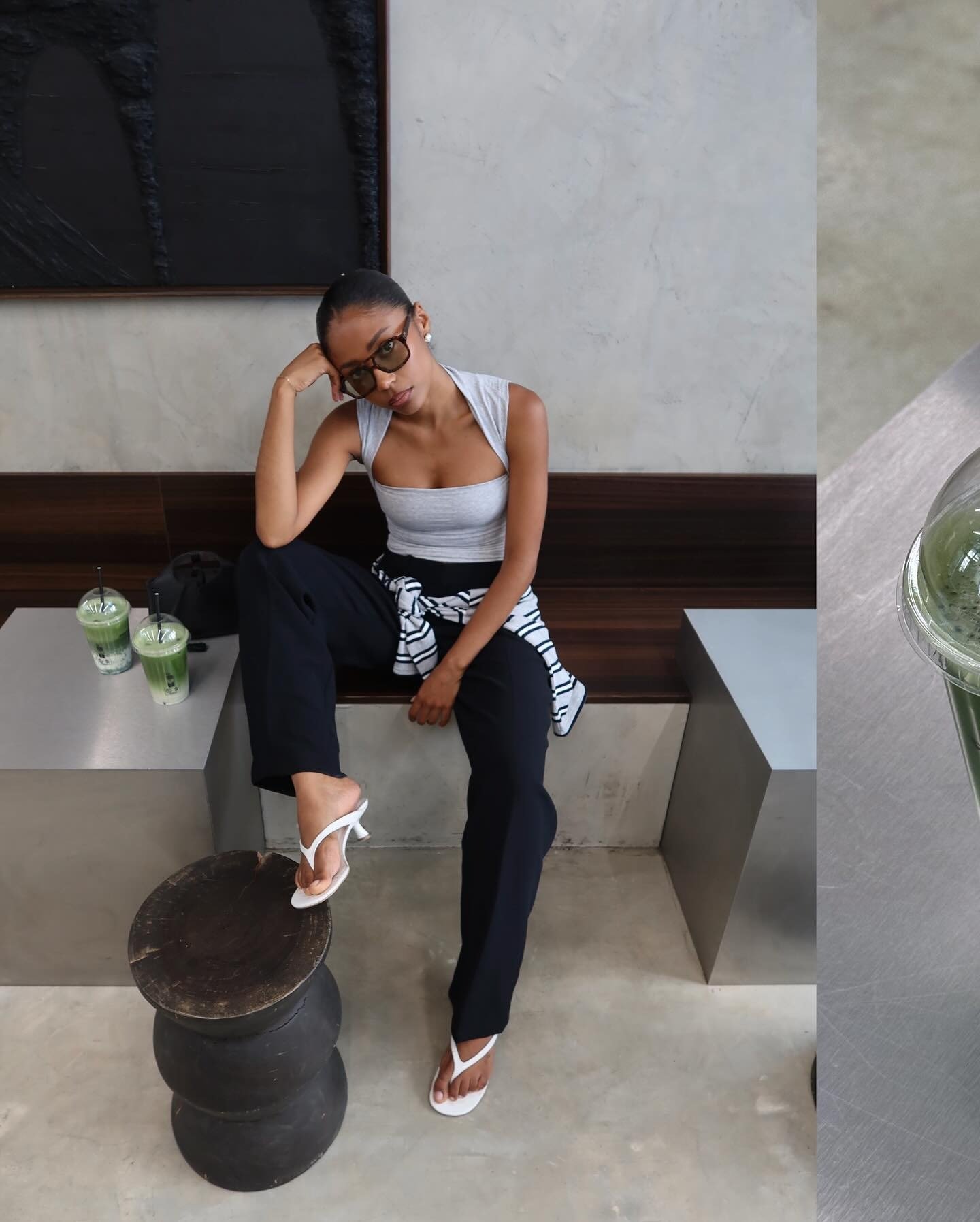 Modelo senta com postura relaxada e olhar confiante, vestindo regata cinza justa, calça preta ampla, sandálias brancas