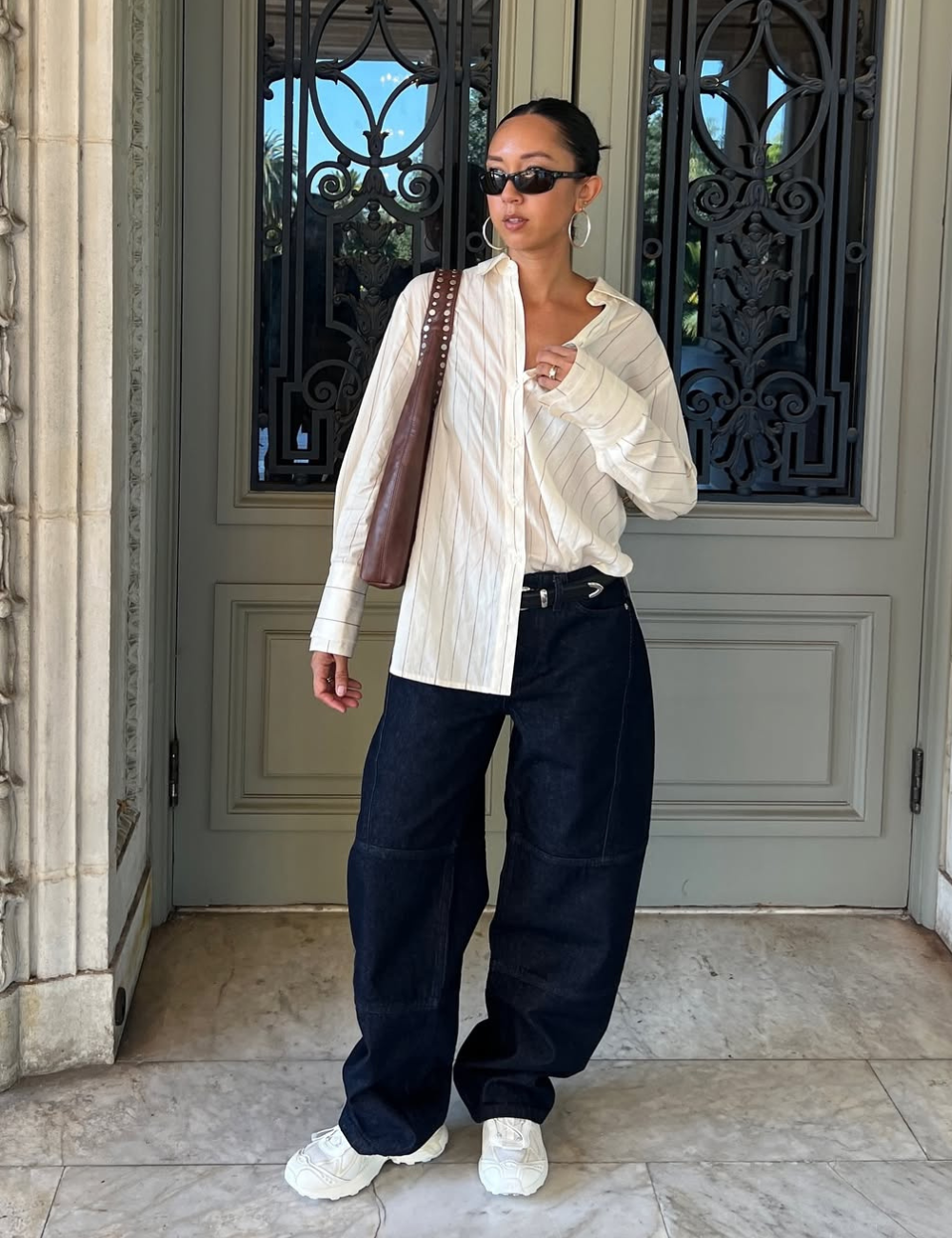 Modelo posa com looks novos e bonitos em camisa branca listrada oversized, calça jeans ampla preta, tênis branco e bolsa.