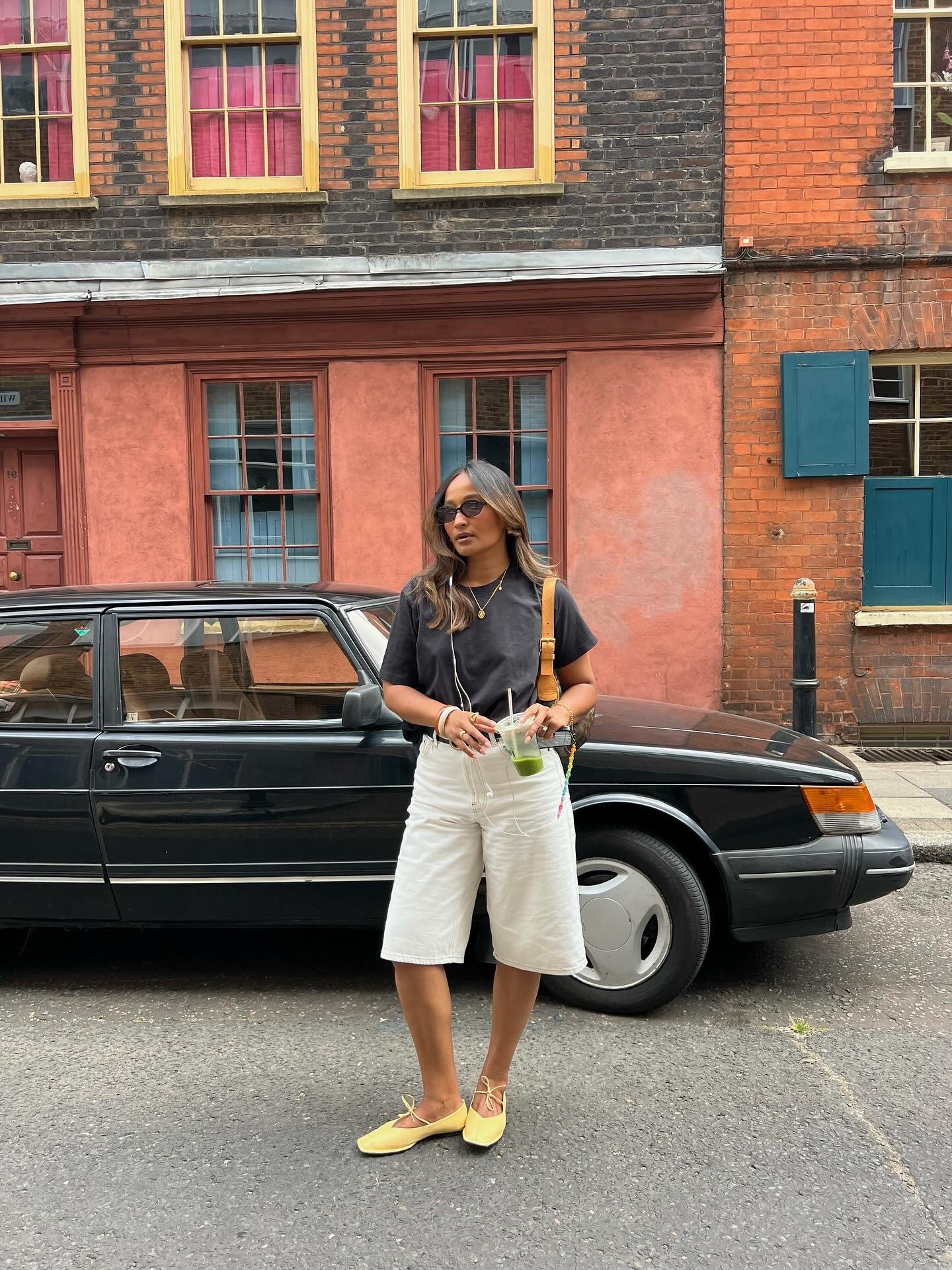 Mulher posa com looks simples e estilosos usando camiseta preta, bermuda branca de tecido leve e sapatilhas amarelas