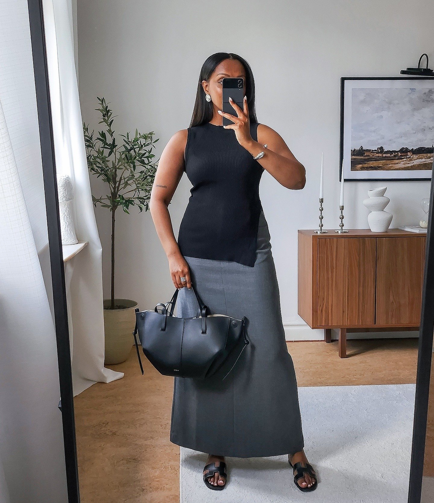 Modelo posa com looks simples e estilosos usando regata preta assimétrica de malha e saia longa cinza de tecido estruturado