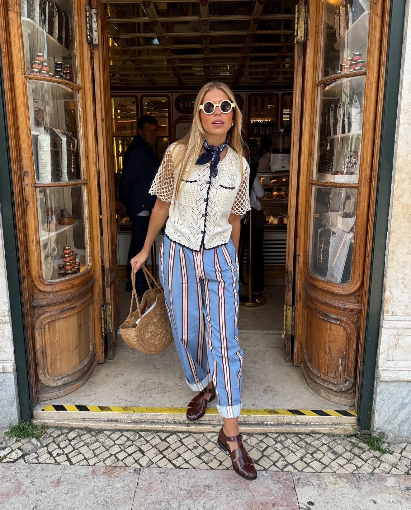 Modelo posa na entrada com looks simples e estilosos, combinando blusa de crochê branca, calça listrada azul e marrom