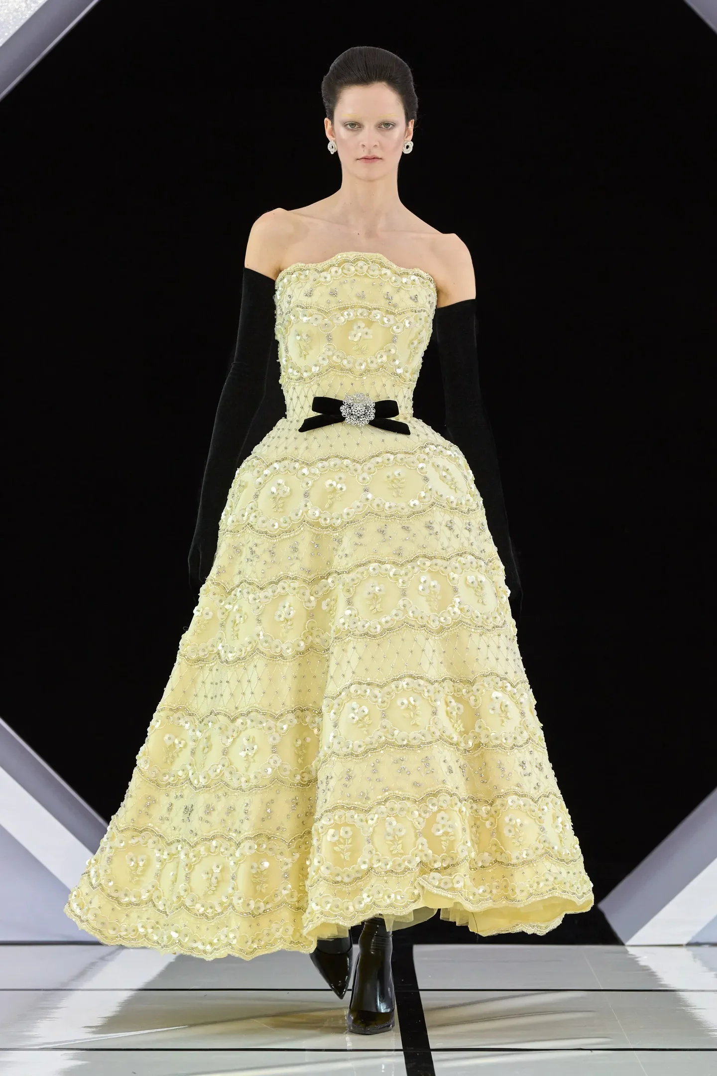 Modelo posa com vestido amarelo bordado e luvas longas pretas de veludo, criando contraste elegante e sofisticado