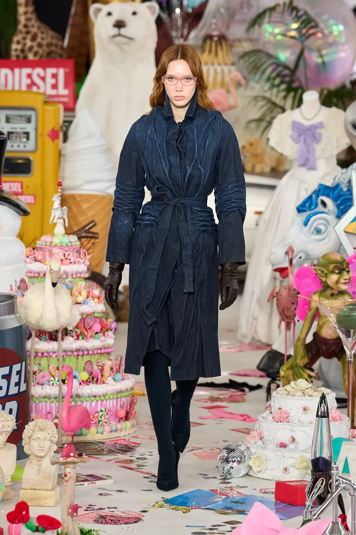 Modelo caminha com postura confiante usando luvas de couro marrom que contrastam com o sobretudo azul escuro de tecido