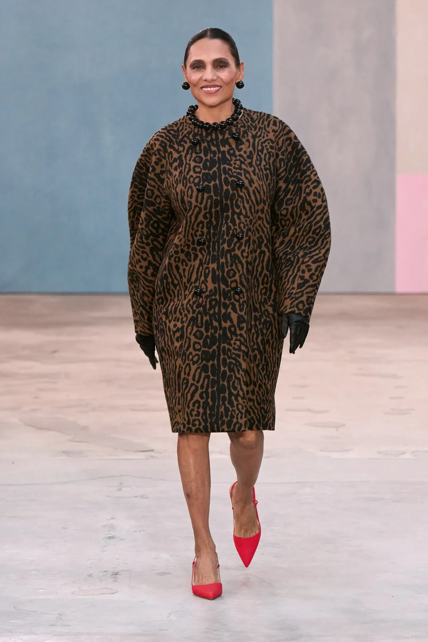 Modelo caminha sorridente com casaco animal print marrom e preto de modelagem ampla, luvas pretas de couro e scarpin