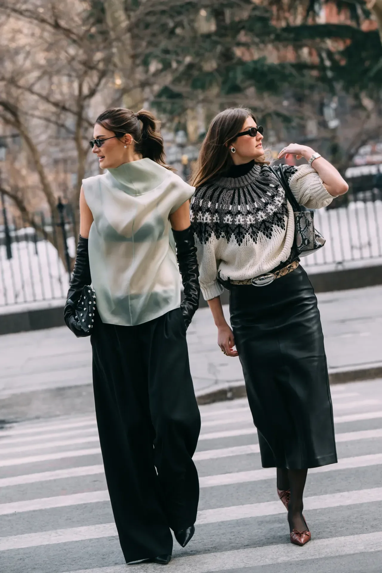 Duas mulheres cruzam a rua com luvas longas de couro preto, combinadas a blusas texturizadas e peças em preto e branco