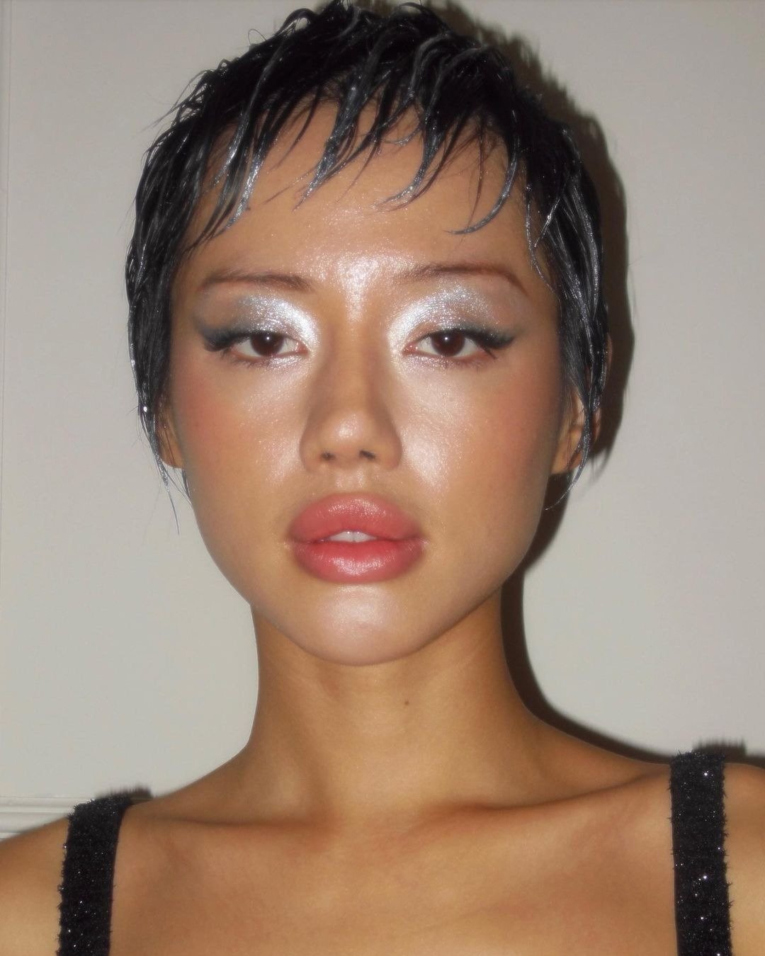 Modelo posa com make de carnaval que destaca sombra prateada cintilante, delineado preto marcante e lábios coral