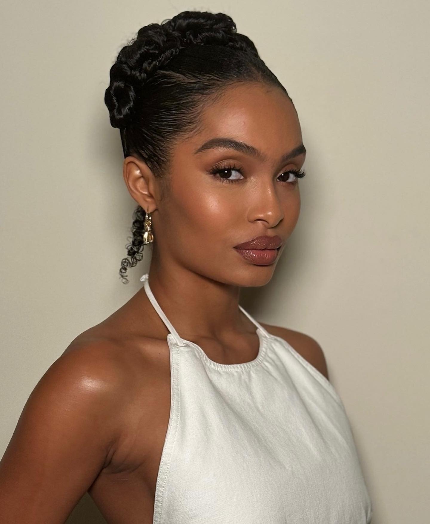 Make de carnaval com pele iluminada, olhos realçados por cílios longos e lábios em tom terroso, cabelo preso em tranças