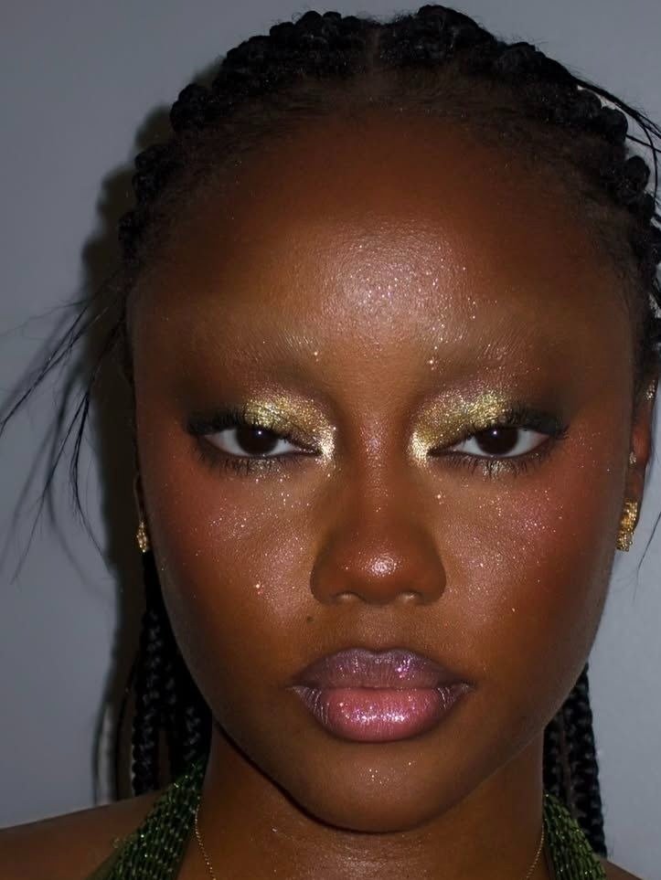 Modelo posa com make de carnaval marcada por sombra dourada cintilante, pele iluminada com glitter e gloss rosado