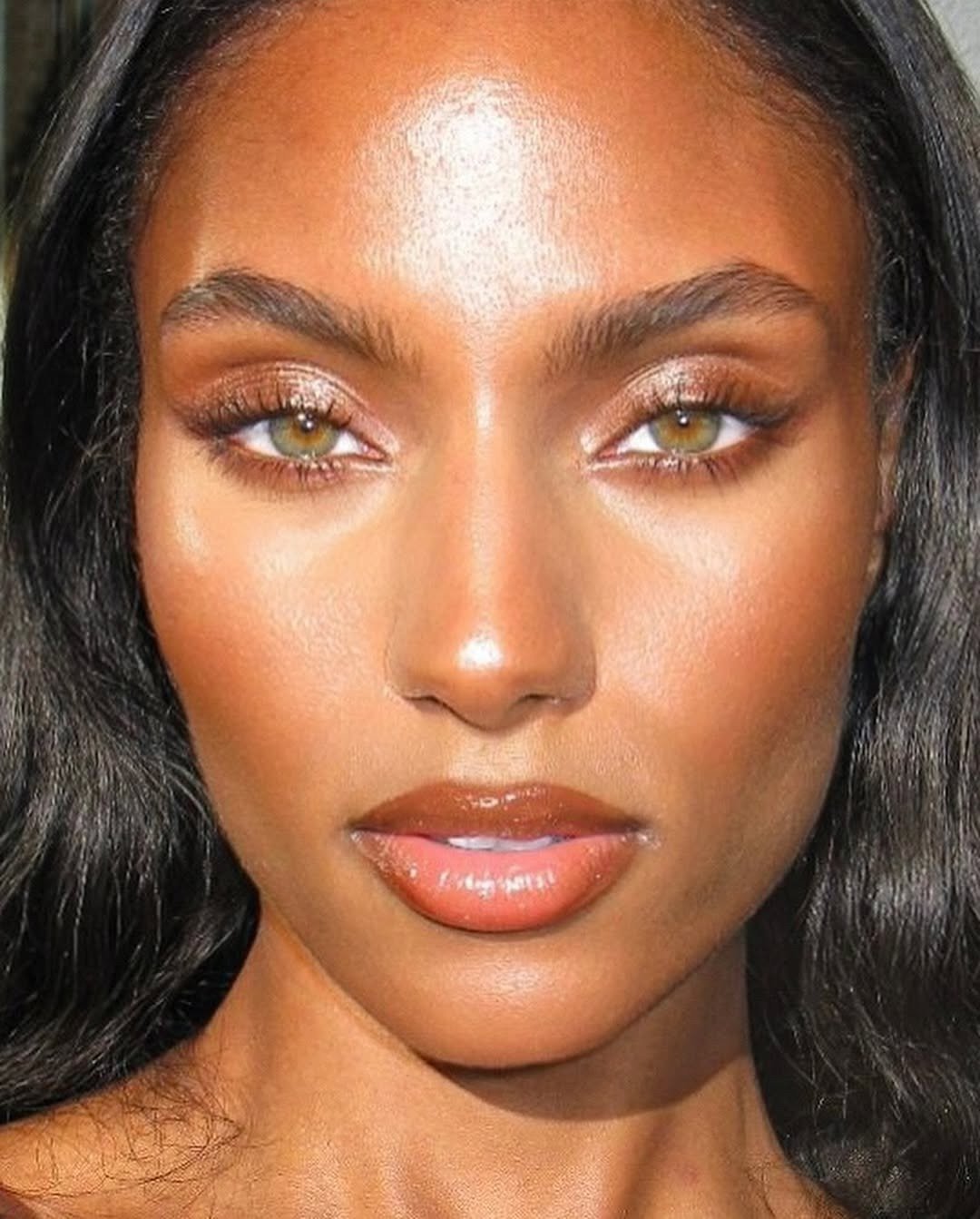 Make de carnaval com pele iluminada, sombras douradas e gloss marrom quente realçando olhos esverdeados e expressão