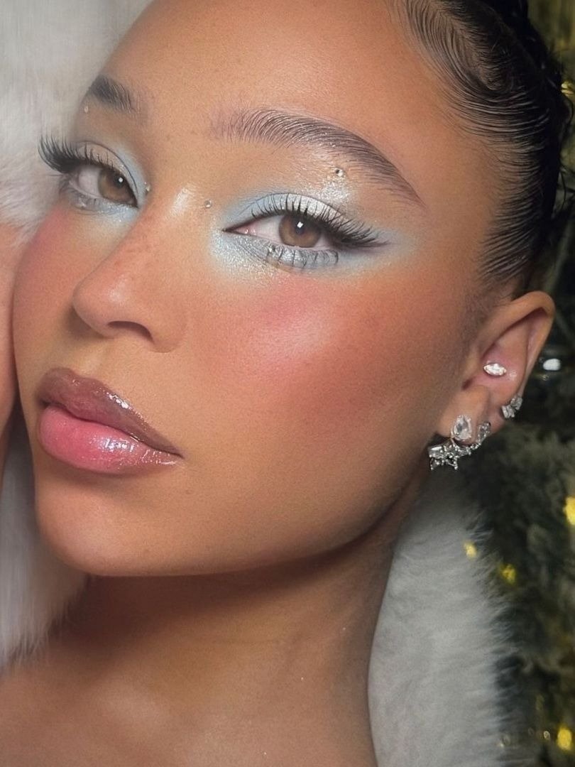 Make de carnaval com sombra azul perolada, cílios longos, pontos de brilho na pele e gloss rosado, realçando delicadeza