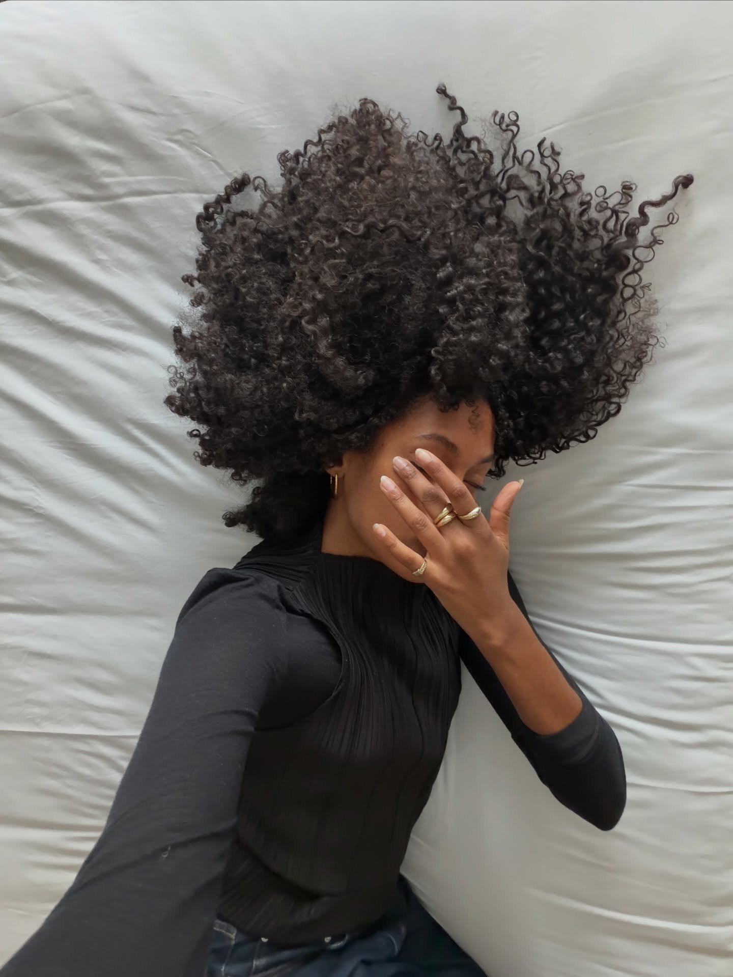 Mulher de blusa preta justa com textura plissada cobre o rosto com a mão, transmitindo introspecção e delicadeza