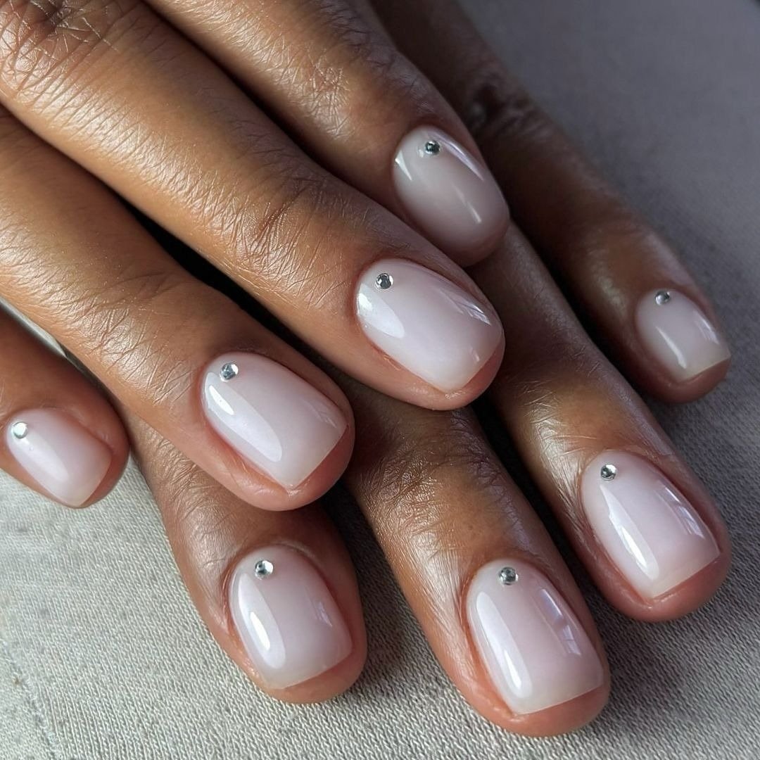 Unhas milky nails curtas com acabamento brilhante e detalhe delicado em strass, realçando a elegância minimalista.