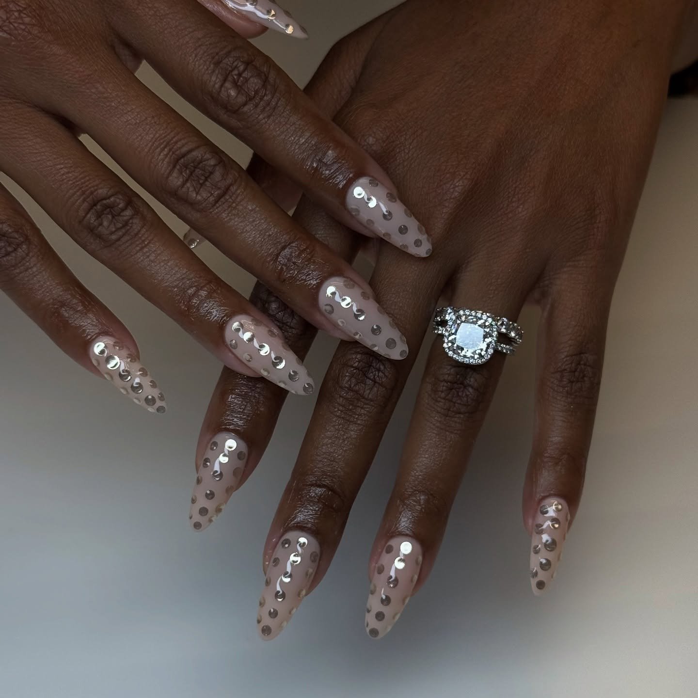 Unhas milky nails alongadas com base nude translúcida e aplicação de paetês prateados, destacando elegância e sofisticação.