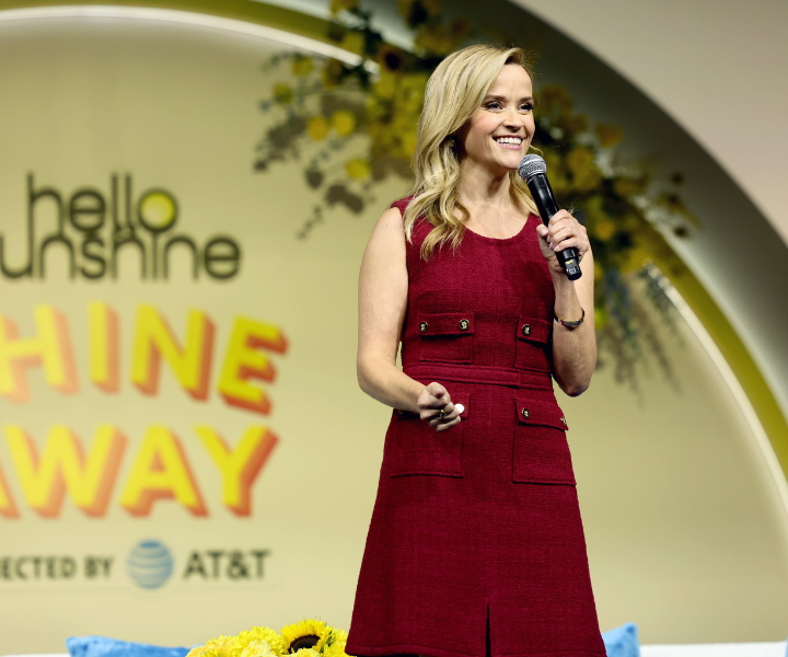 Atriz e produtora veste vestido vinho texturizado com bolsos frontais, posa sorridente e confiante em evento iluminado.