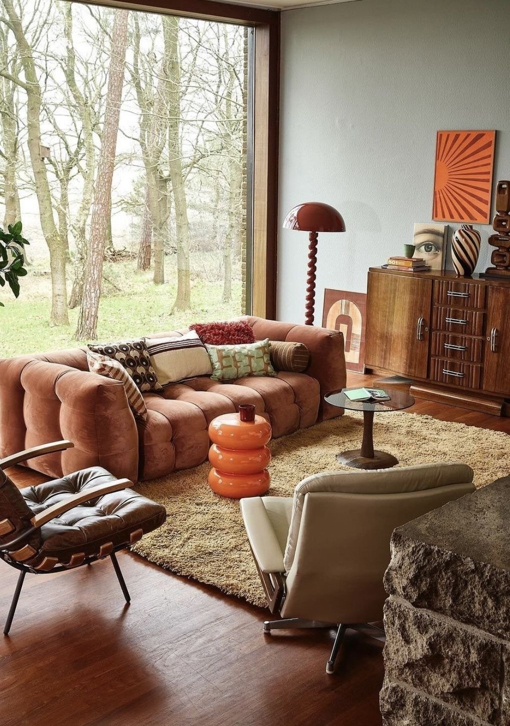 Sala neo déco com sofá de veludo terracota, poltronas em couro marrom e bege, luminária vermelha e móveis em madeira