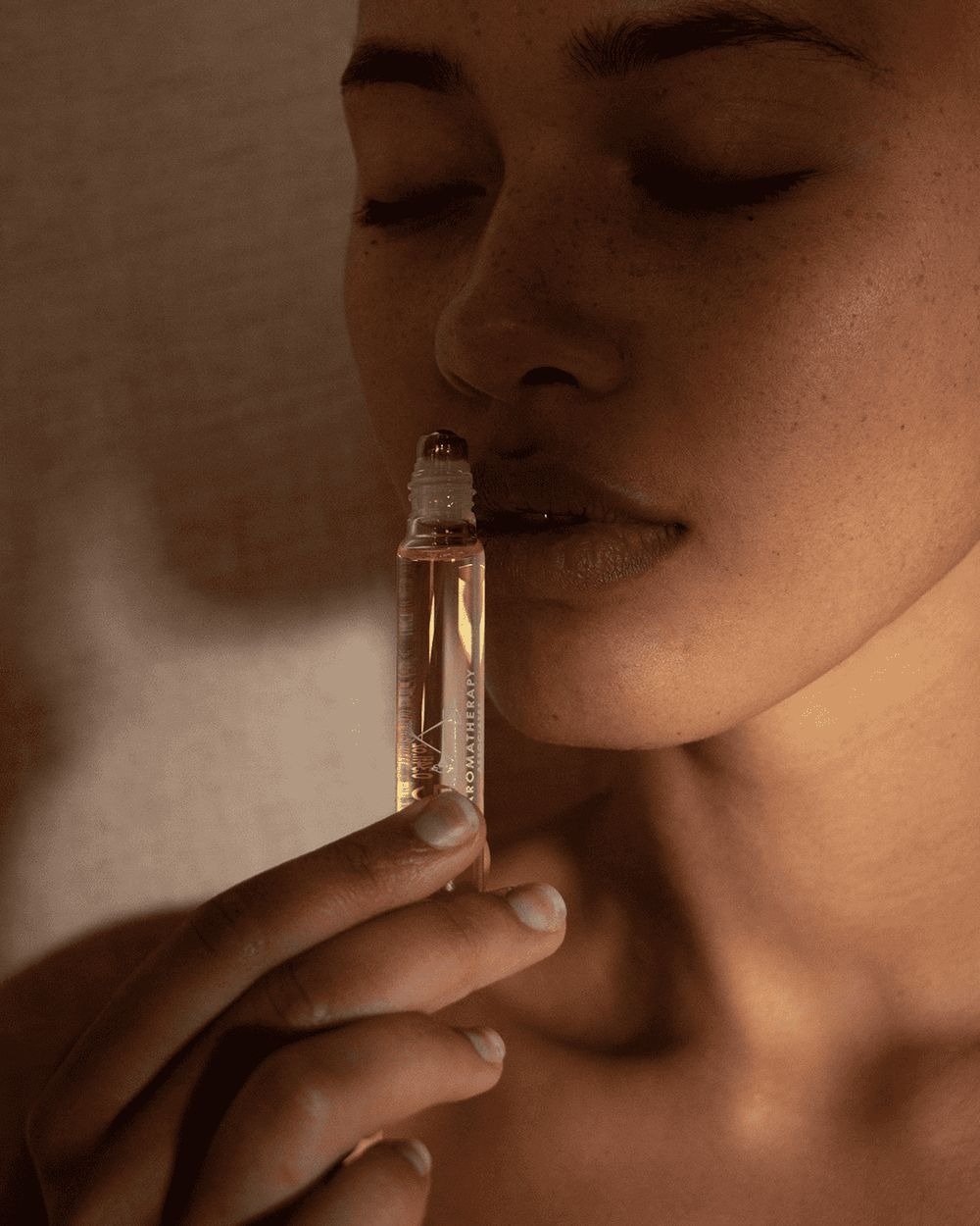 Mulher com expressão serena segura frasco de vidro transparente com rolon, sugerindo o melhor óleo essencial