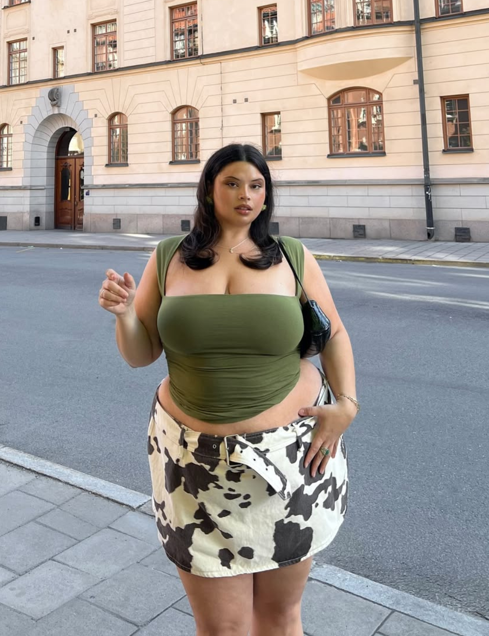 Modelo posa confiante na moda do verão 2026 com top verde musgo justo de alças largas e minissaia de estampa animal.