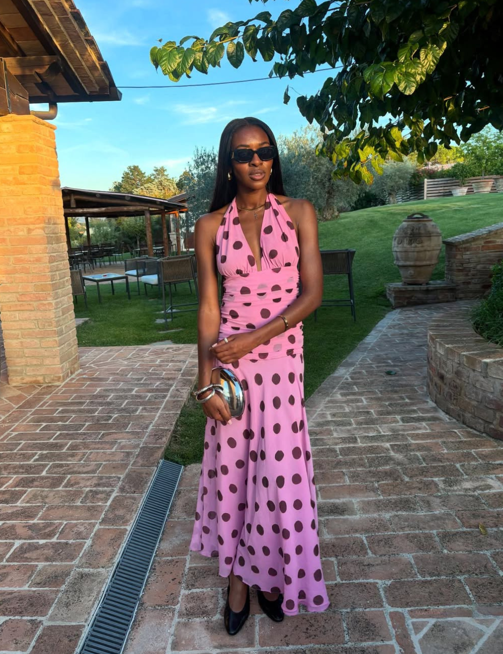 Modelo posa com vestido longo rosa de poás marrons, decote halter e tecido fluido, destacando a elegância leve do verão.