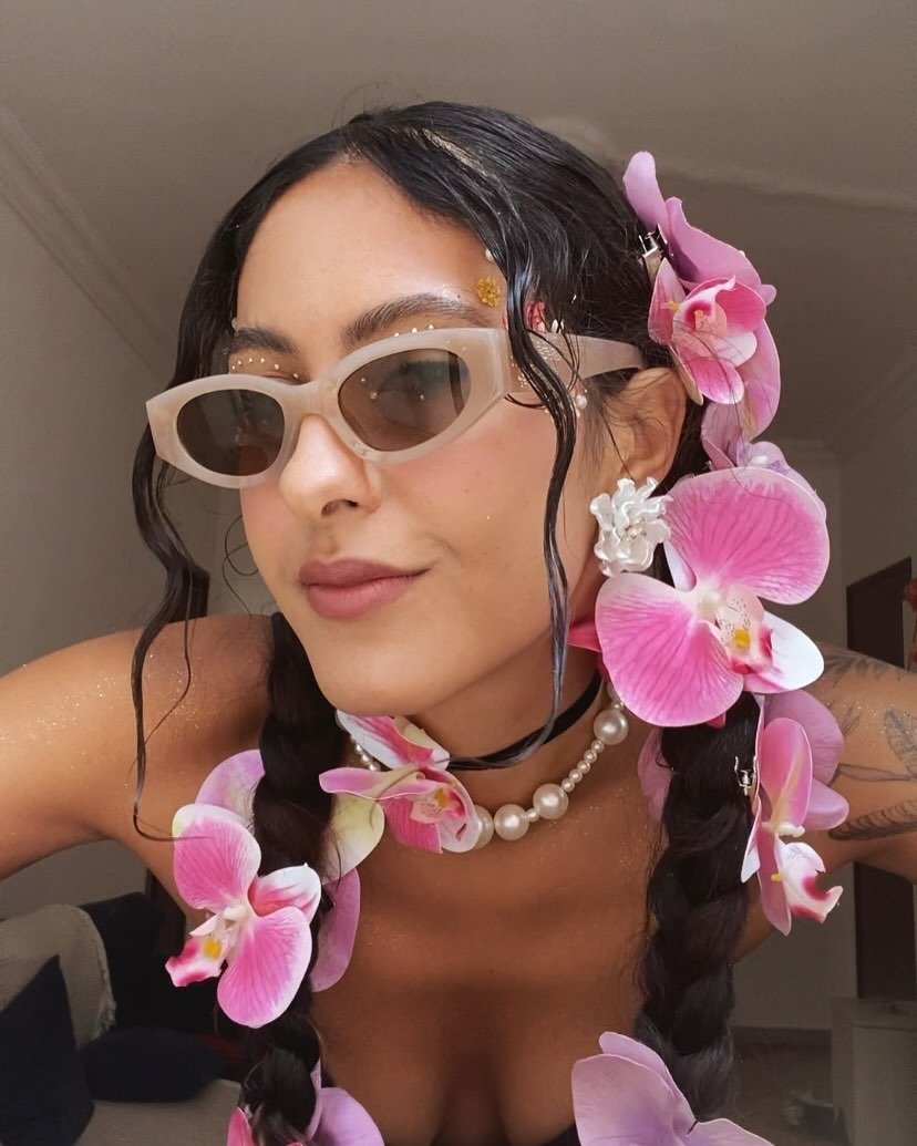 Penteado para Carnaval simples com tranças decoradas por flores orquídeas rosa, acessórios perolados e estilo descontraído e