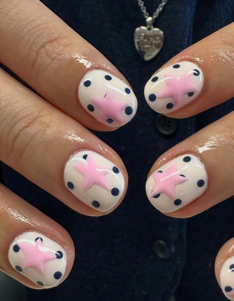 Unha de bolinhas preta sobre base branca com estrela 3D rosa, destacando textura brilhante e estilo divertido e delicado.