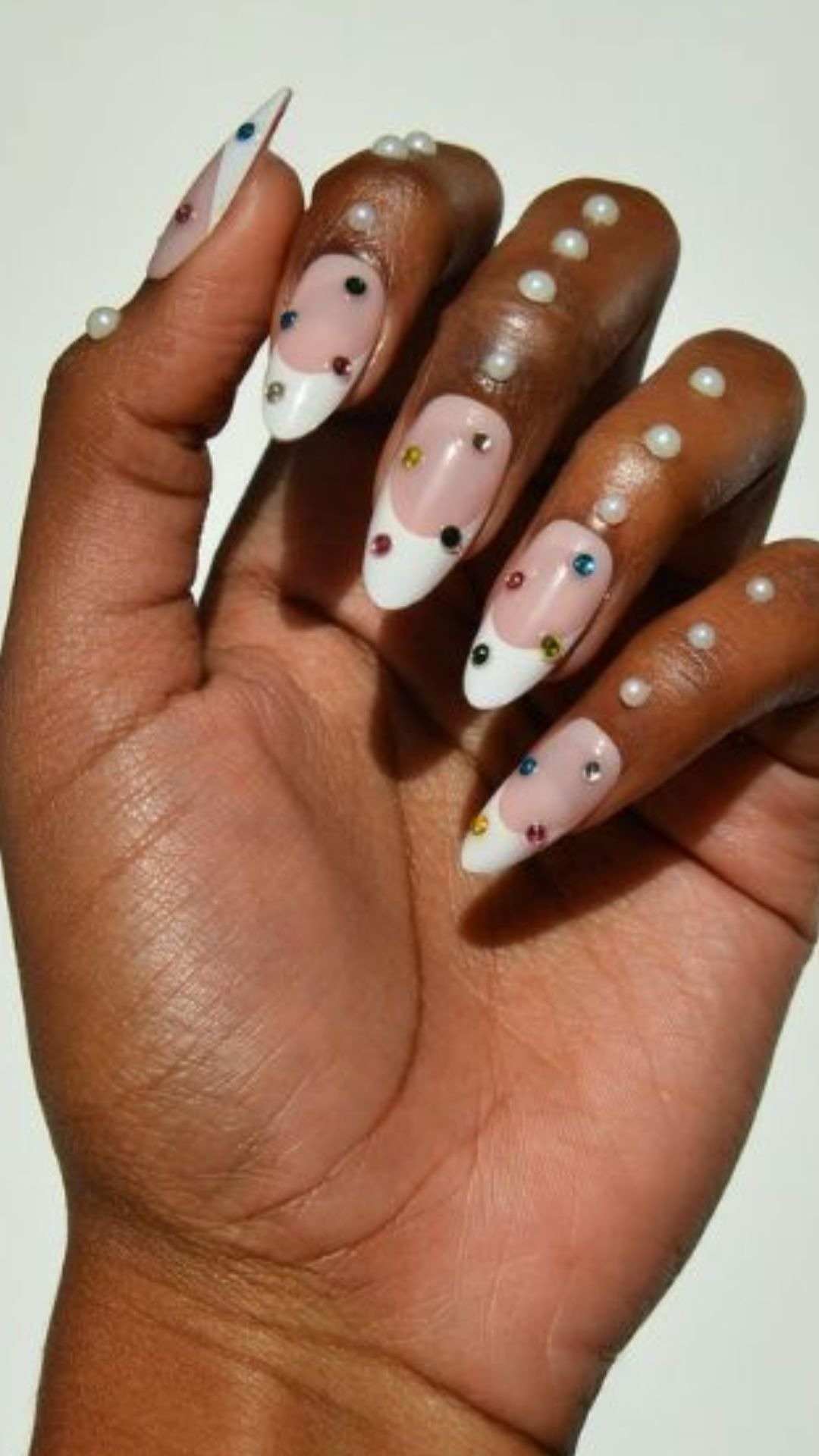 Unha de bolinhas com base nude e ponta branca em formato stiletto, decorada com pedrinhas coloridas e pérolas sobre pele