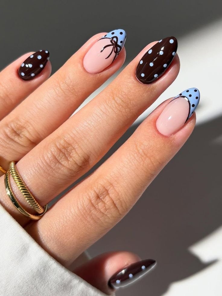 Unha de bolinhas com esmalte marrom e azul claro, detalhes em laço preto, formato oval e acabamento brilhante 