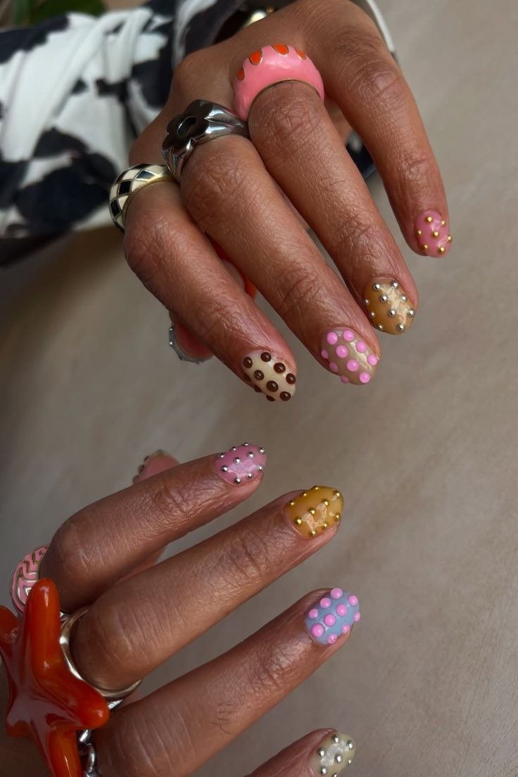 Unha de bolinhas em tons pastel e terrosos com texturas em relevo, combinando anéis prateados e clima moderno e artístico.