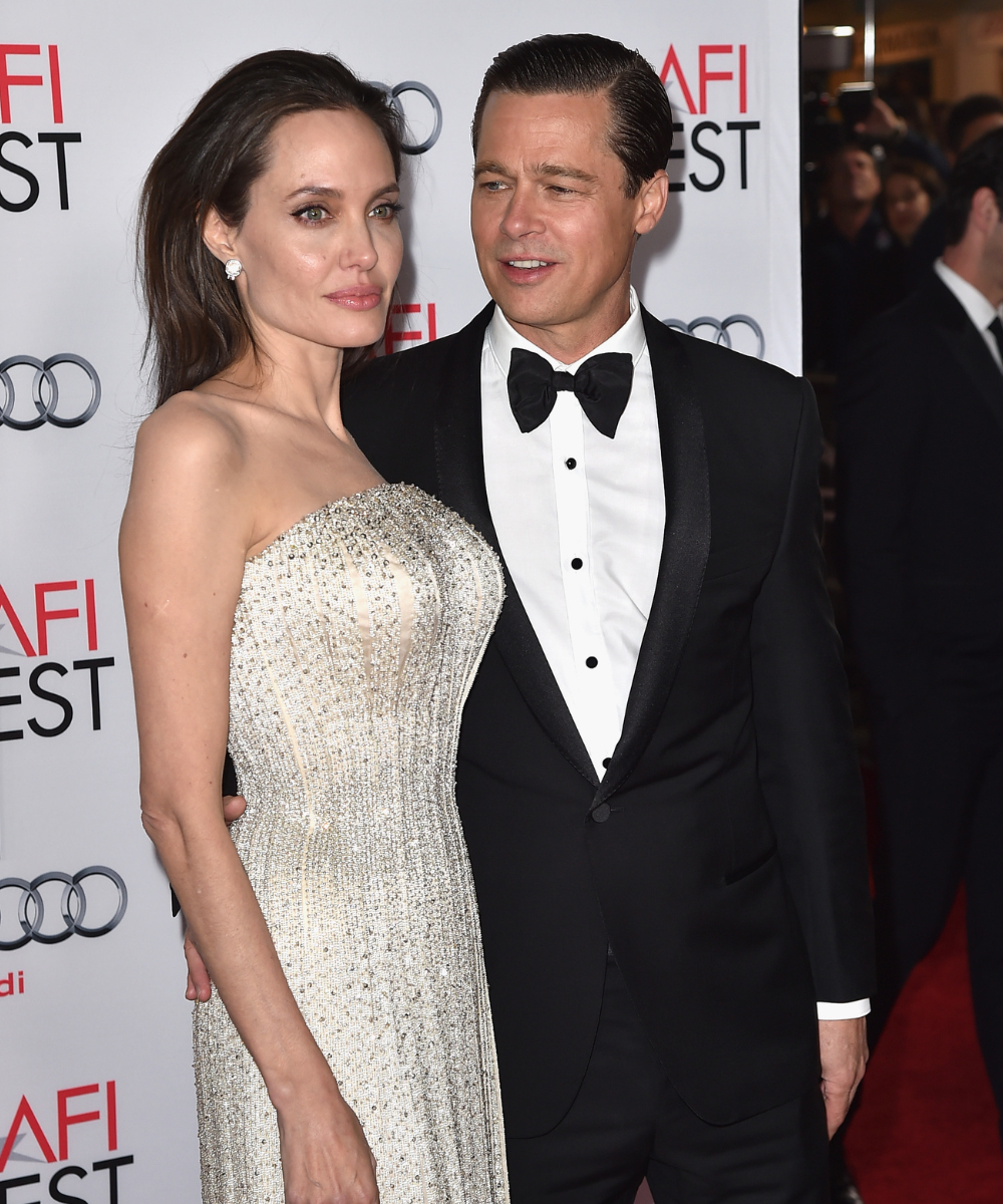 Casal posa em tapete vermelho com vestido tomara que caia bordado em prata e smoking preto clássico, evocando romance