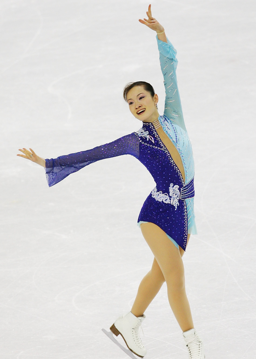 Patinadora artística em pose elegante exibe vestido bicolor azul com brilho e renda, irradiando graça e leveza na patinação.