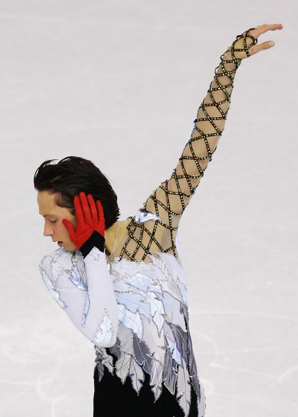 Patinador artístico veste traje branco com detalhes prateados e manga nude com tiras pretas.
