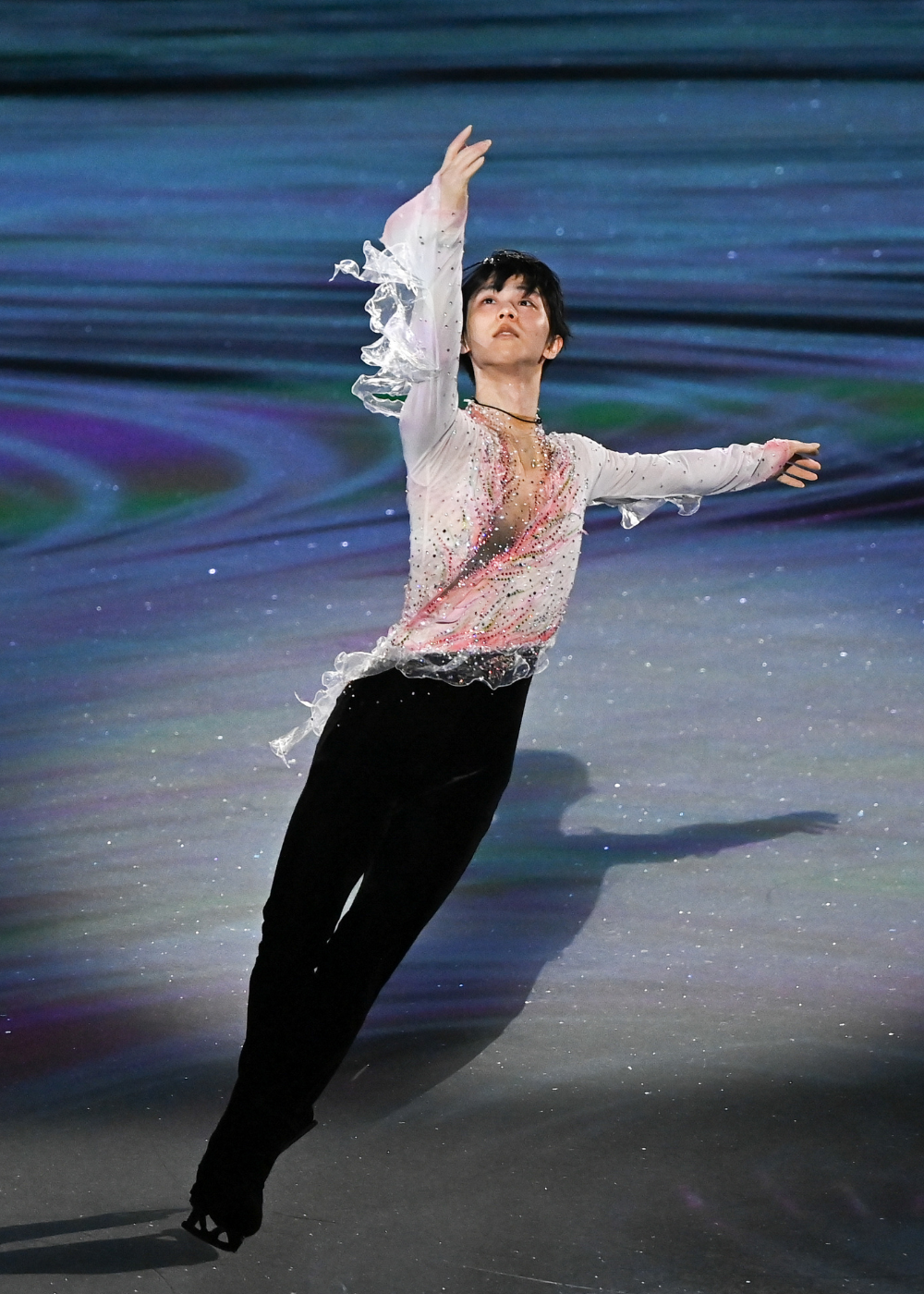 Patinação artística com traje fluido branco e rosa em tecido translúcido e brilhos, modelo executa movimento elegante.