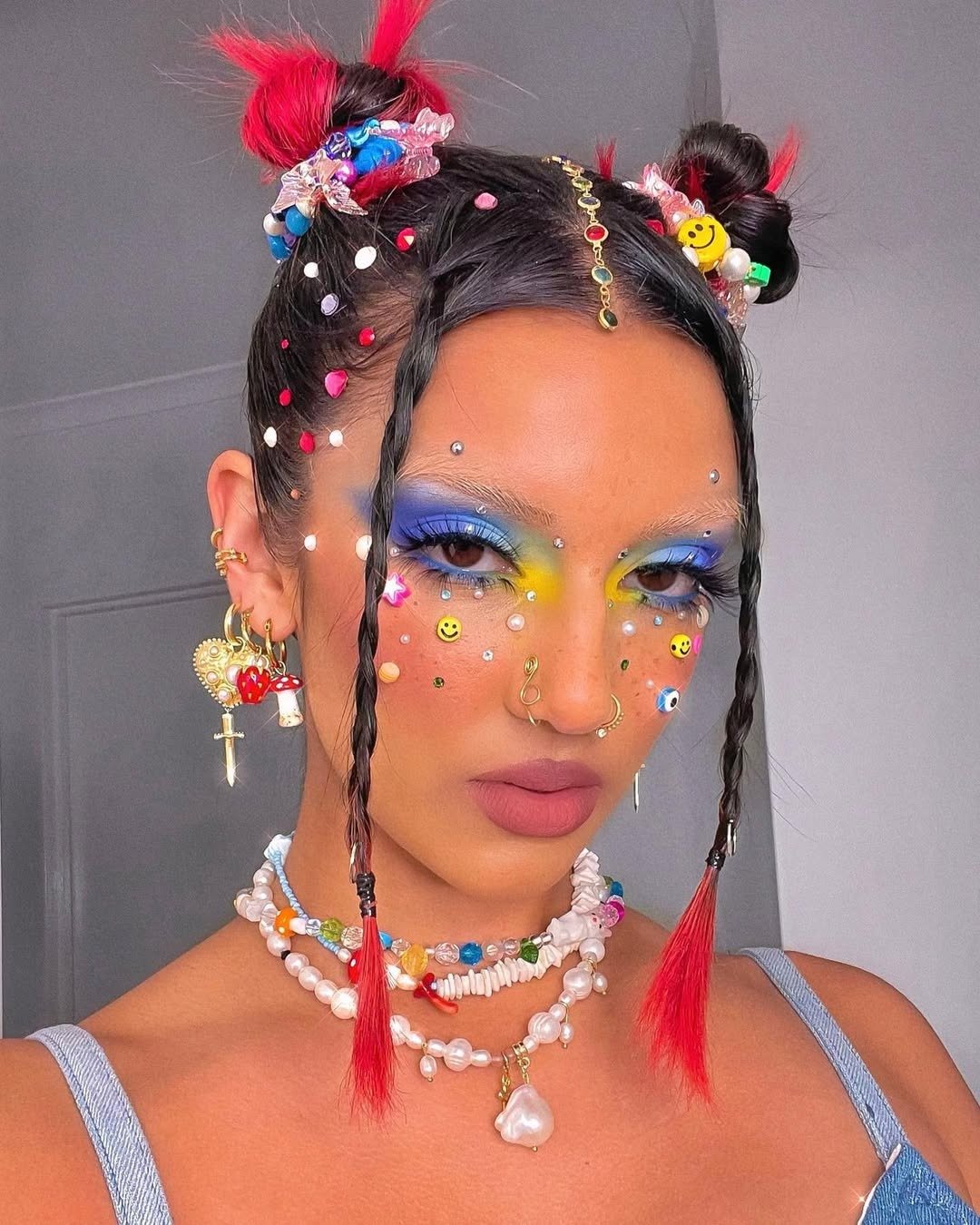 Penteado para Carnaval simples com dois coques altos adornados por penas vermelhas, miçangas coloridas e tranças frontais