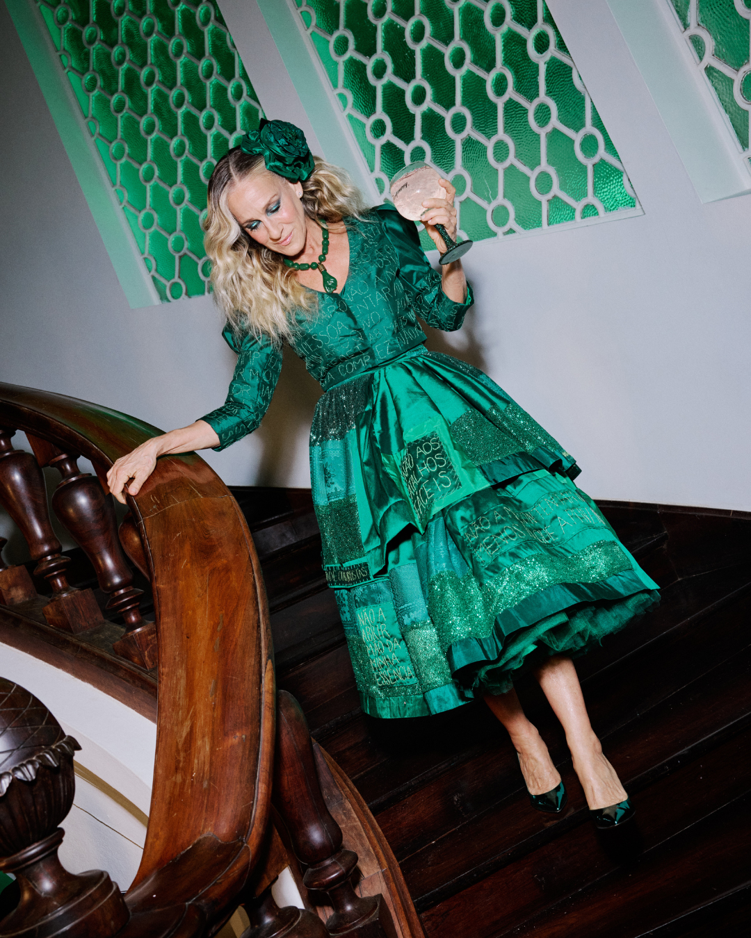 Mulher desce escada com vestido verde patchwork de tecidos brilhosos e bordados, postura confiante celebra saber dizer “não”