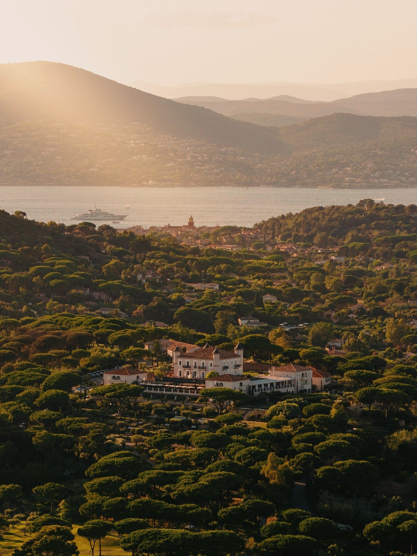 Paisagem de Saint-Tropez ao entardecer com tons dourados, arquitetura mediterrânea e vegetação densa em clima sereno