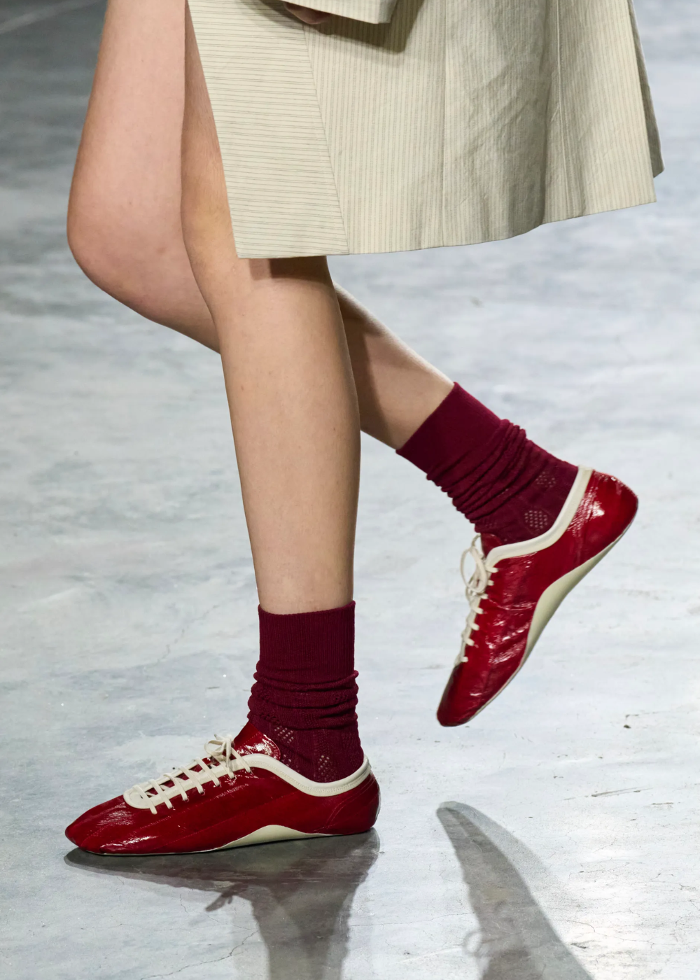 Sapatos flat vermelhos em material brilhante combinam com meias vinho e saia bege de tecido leve.