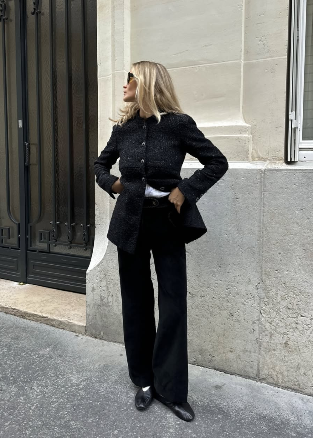 Modelo posa com postura confiante usando sapatos flat pretos de couro, calça reta e blazer texturizado.