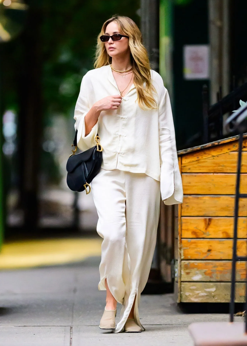 Modelo caminha com postura confiante usando sapatos flat bege combinados a conjunto fluido branco de tecido leve.