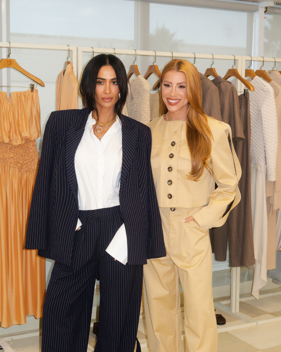 Silvia Braz posa com blazer oversized listrado e calça ampla, ao lado de mulher em conjunto bege estruturado,