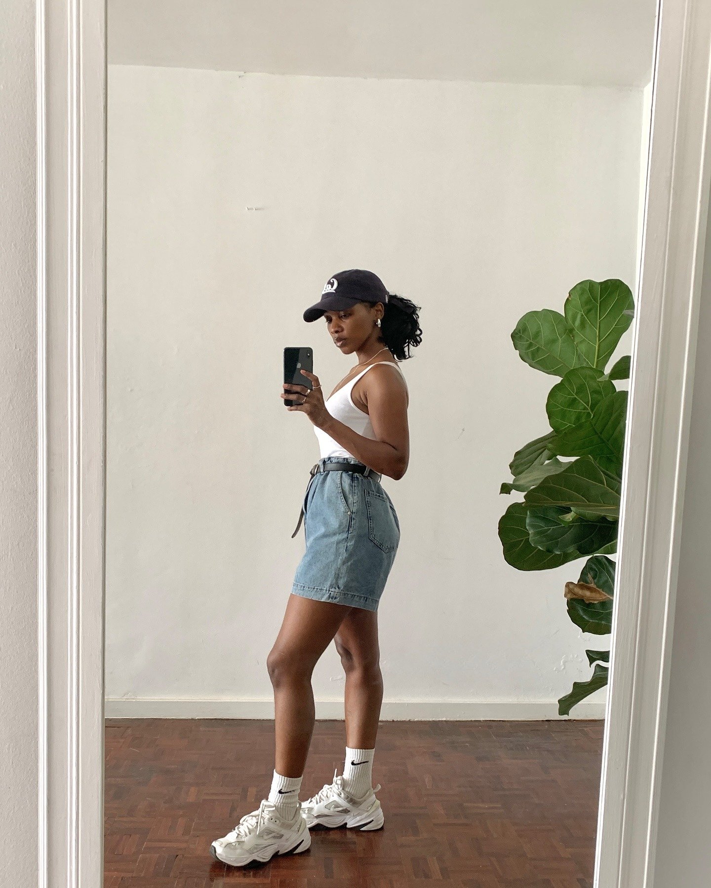 Modelo posa de perfil com sneaker feminino branco de solado robusto, meia branca, saia jeans clara e regata branca