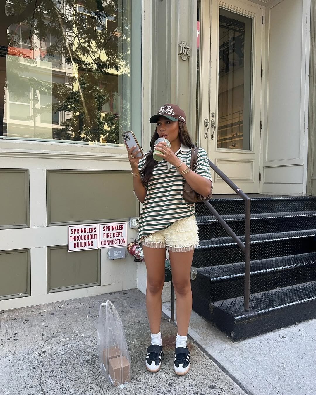 Mulher em postura casual usa sneaker feminino preto e branco com meias, short de babados creme e camiseta listrada verde