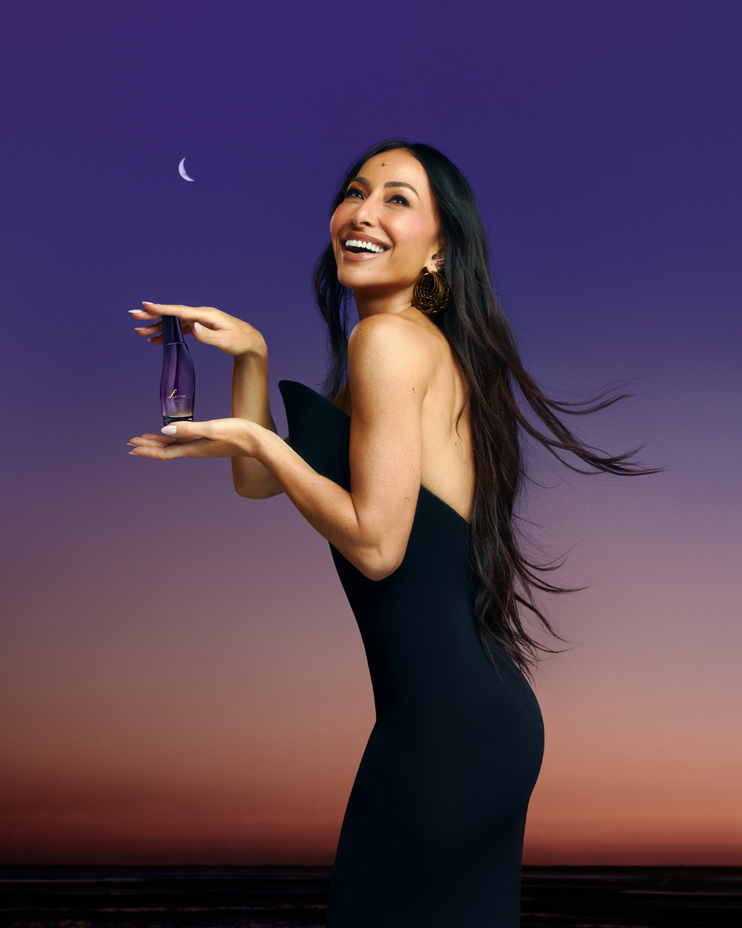 Modelo sorri olhando para cima, veste vestido preto justo sem mangas e segura perfume roxo, evocando fragrâncias intensas