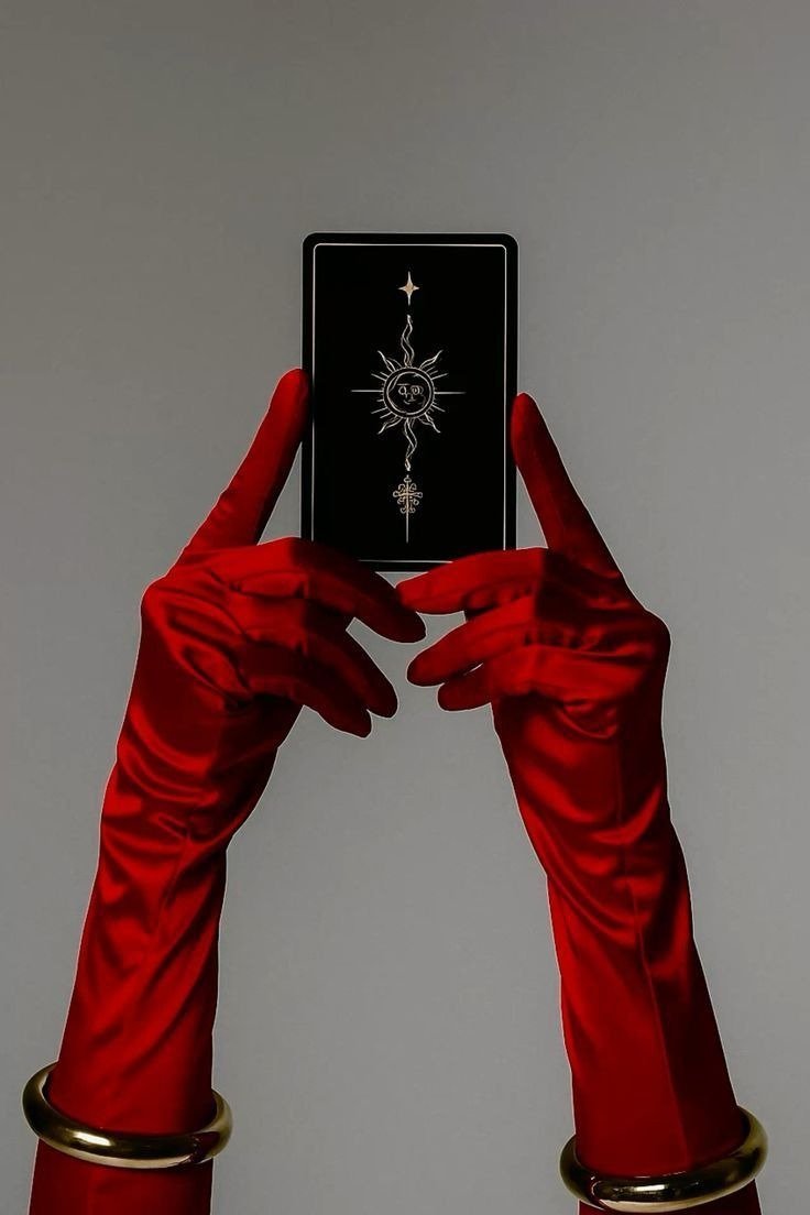 Mãos com luvas vermelhas de cetim e braceletes dourados seguram carta preta com sol. Conselho do tarot para cada signo